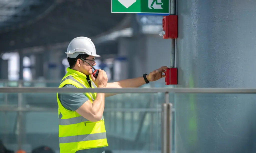 Engineer wearing safety unifrom and helmet under checking fire alarm emergency system in industry factory and exit door is factory security protection concept.