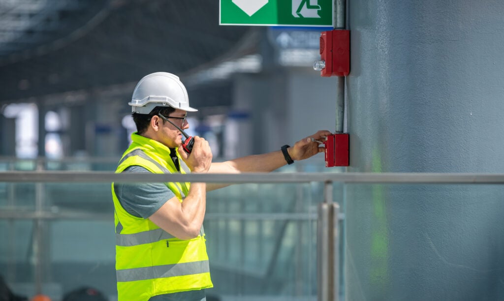 Engineer wearing safety unifrom and helmet under checking fire alarm emergency system in industry factory and exit door is factory security protection concept.